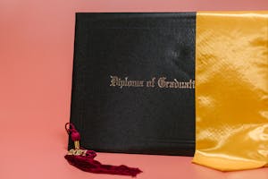 Black diploma with garnet tassel and gold sash symbolizes academic achievement.